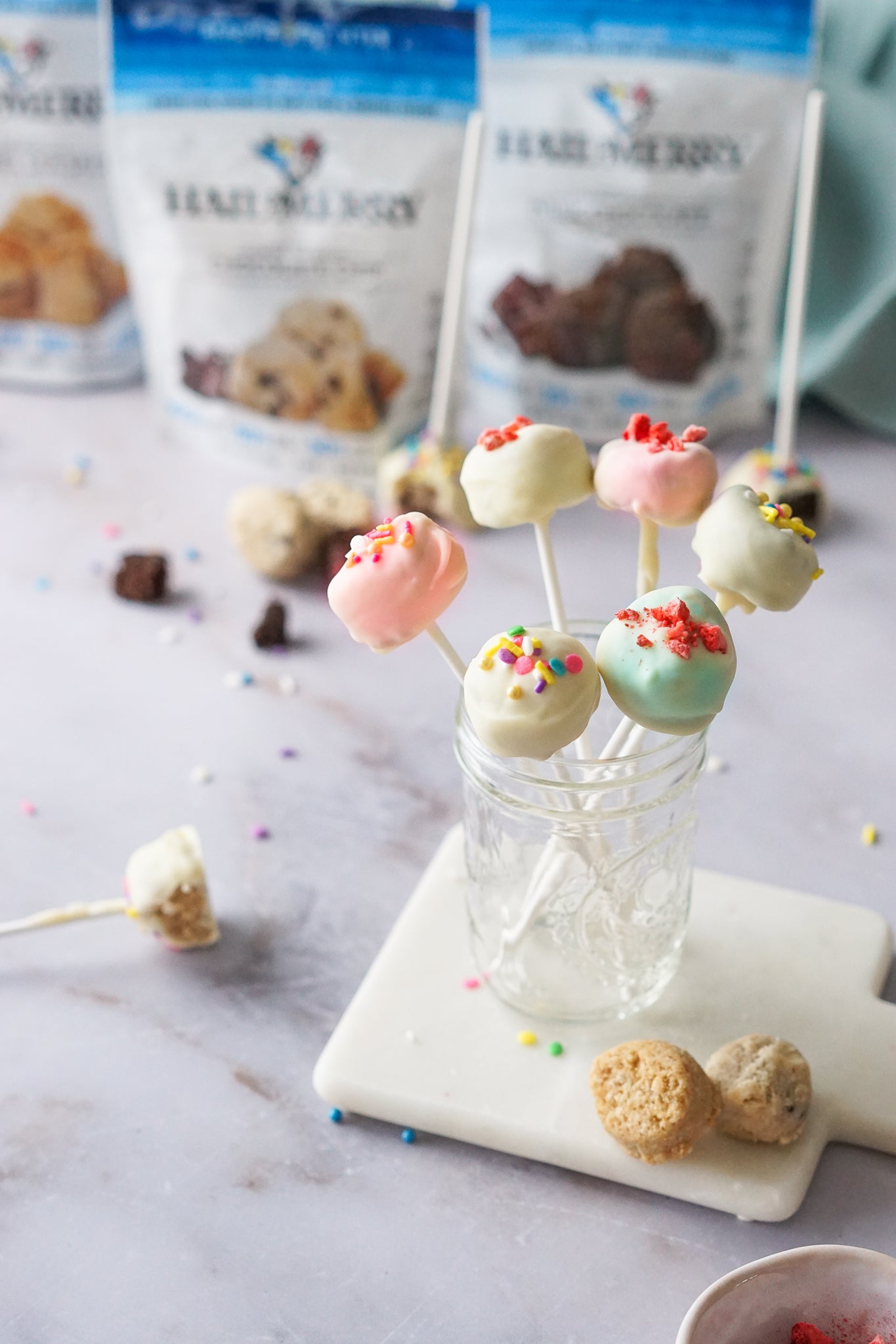Coconut cookie dough pops featuring plant-based caramel sea salt cookie dough, dipped in vegan white chocolate and topped with natural sprinkles and freeze-dried strawberries.